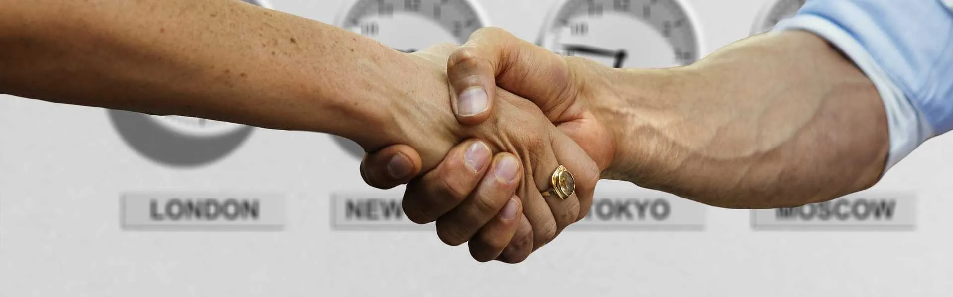 Two people shaking hands in front of world-time clocks for London, New York, Tokyo and Moscow